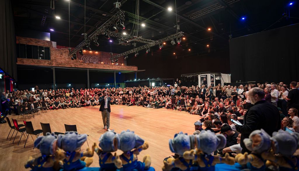 audience2 A man holding two stuffed toy mouse figures, standing in front of an audience